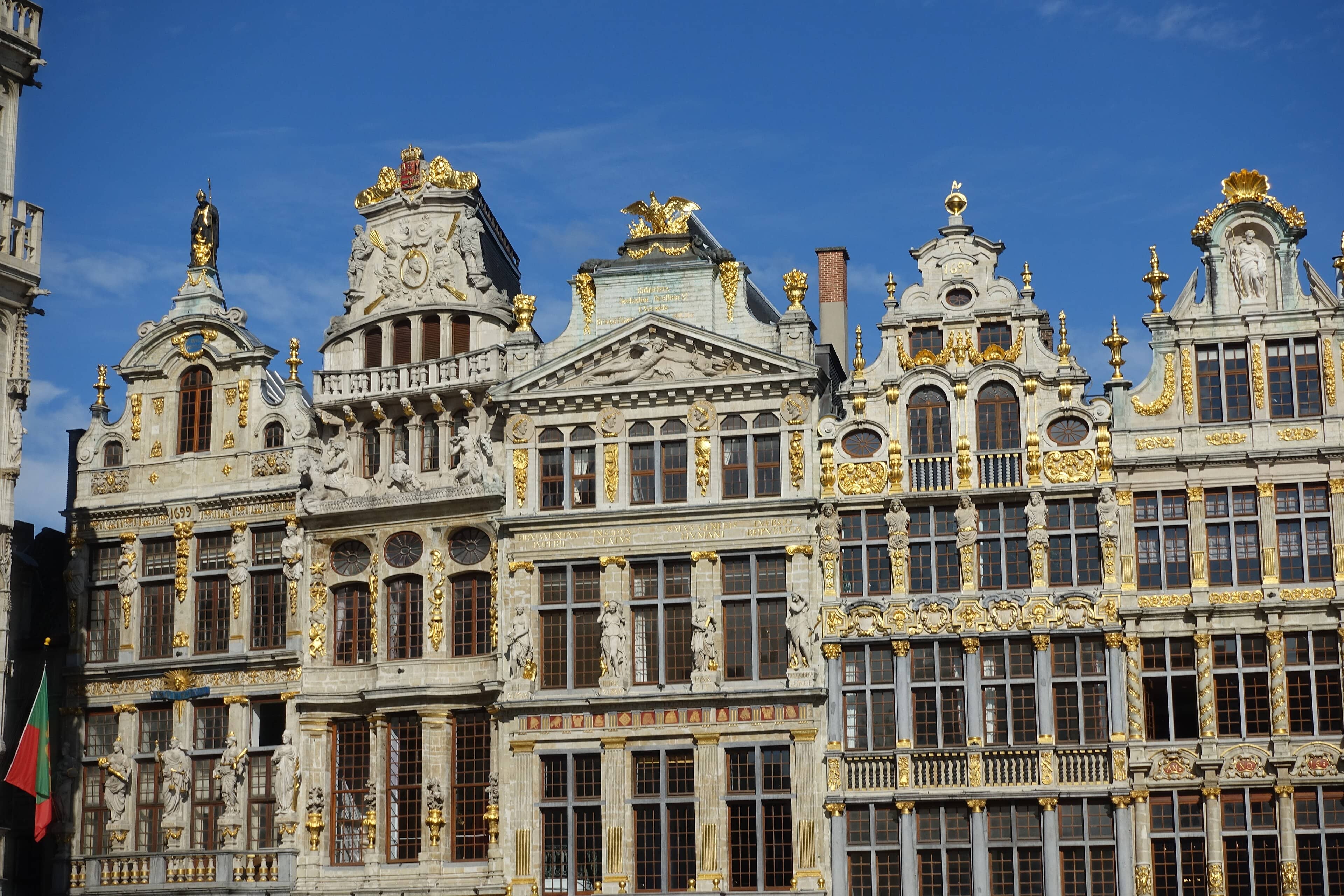 Gilded guildhall façades of Brussels' Grand-Place glowing in bright sunshine against a blue sky.</alt>