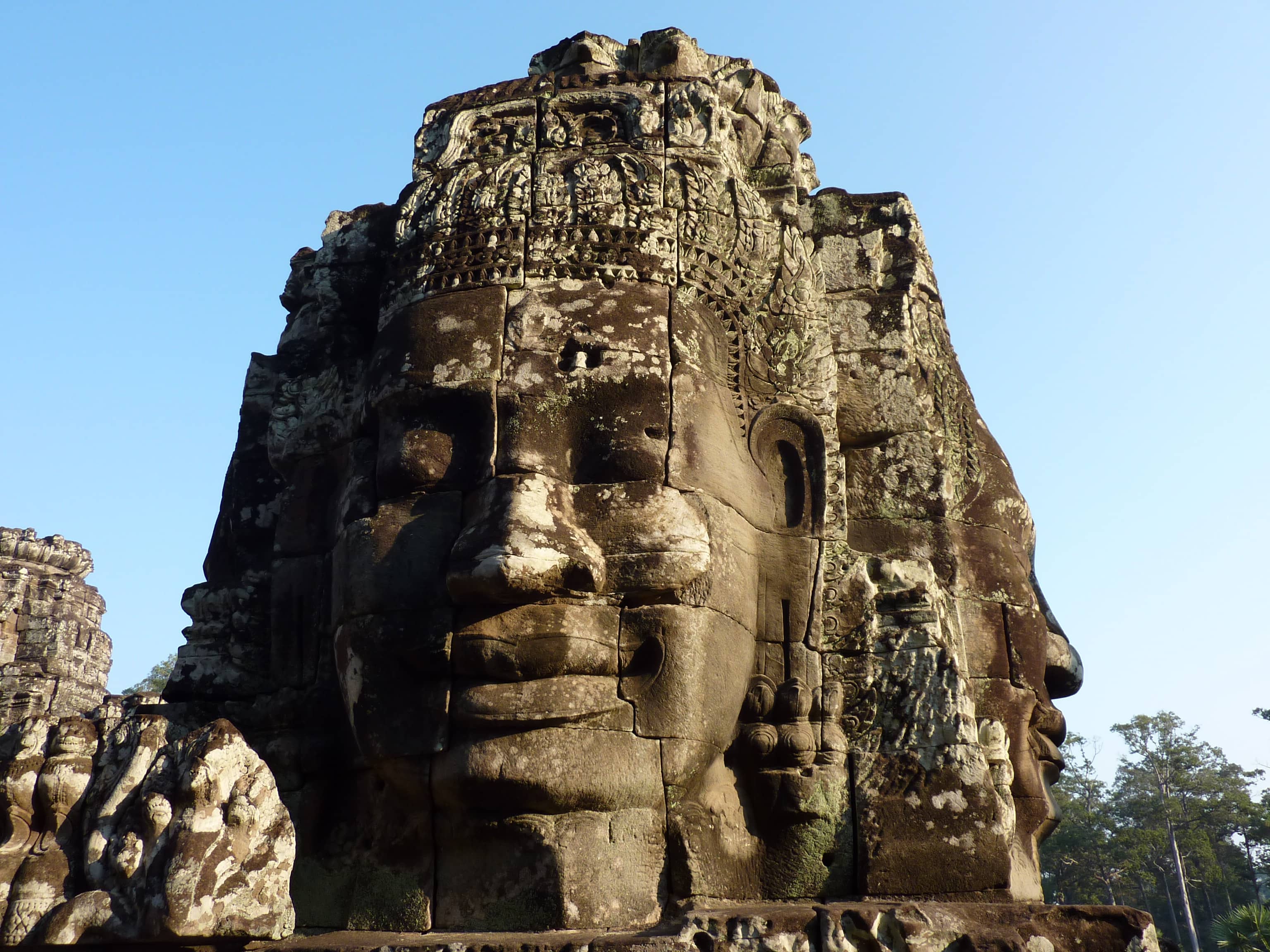 Sunlit stone face tower at the Bayon temple, Angkor, against a clear blue sky in Cambodia