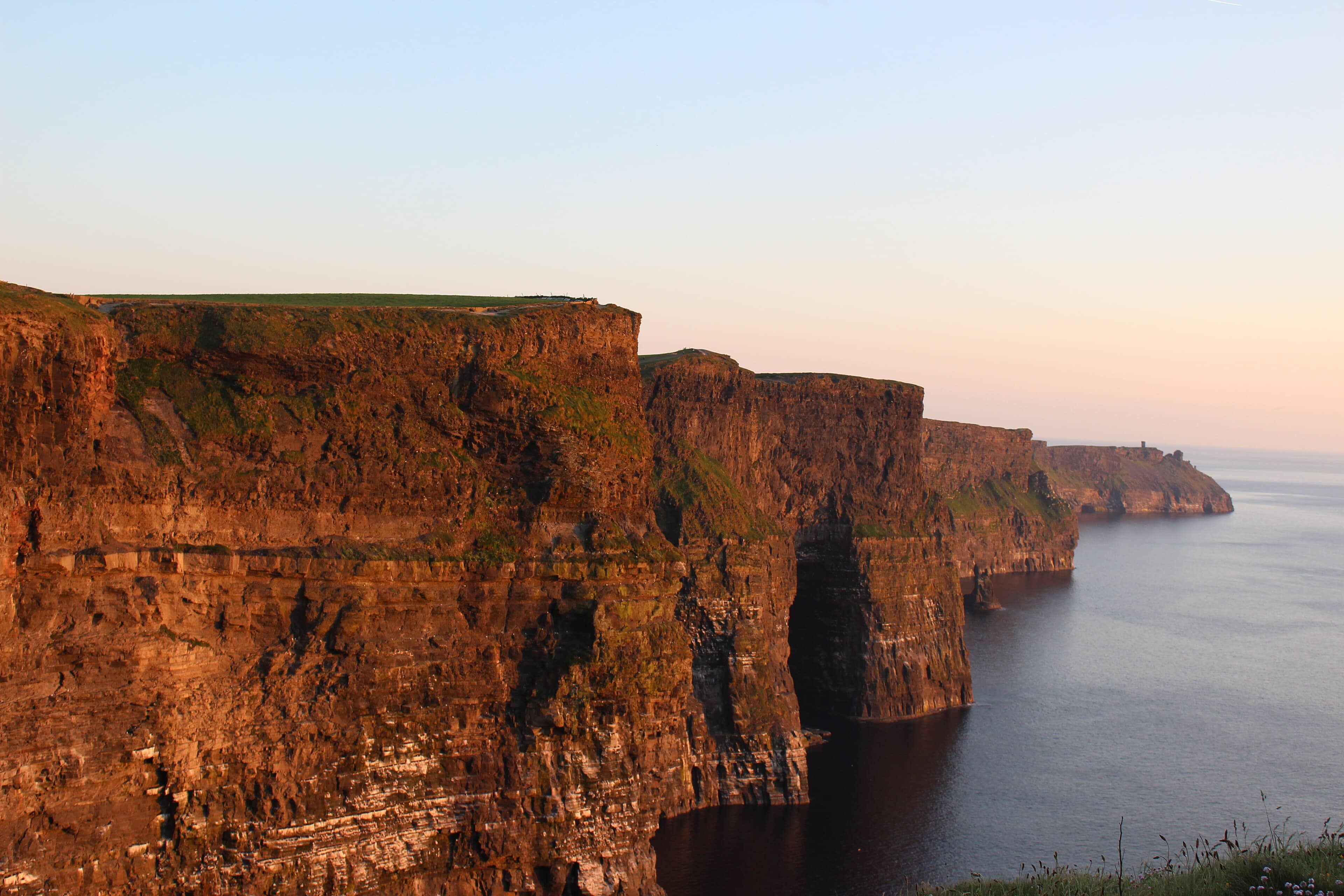 Warm light on the layered Cliffs of Moher above a calm Atlantic Ocean, County Clare, Ireland