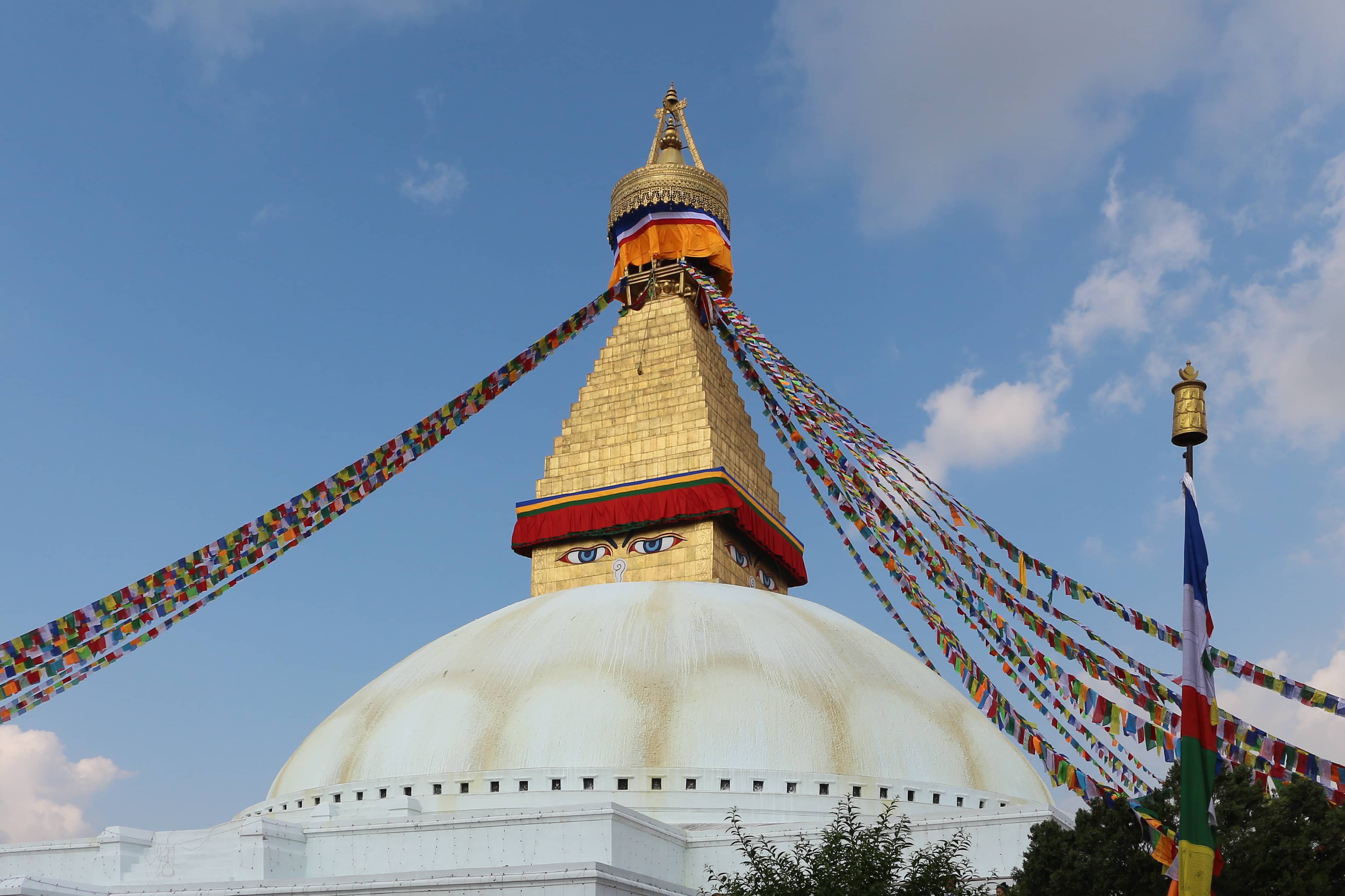 The golden spire and prayer flags of Boudhanath Stupa in Kathmandu against a bright blue sky