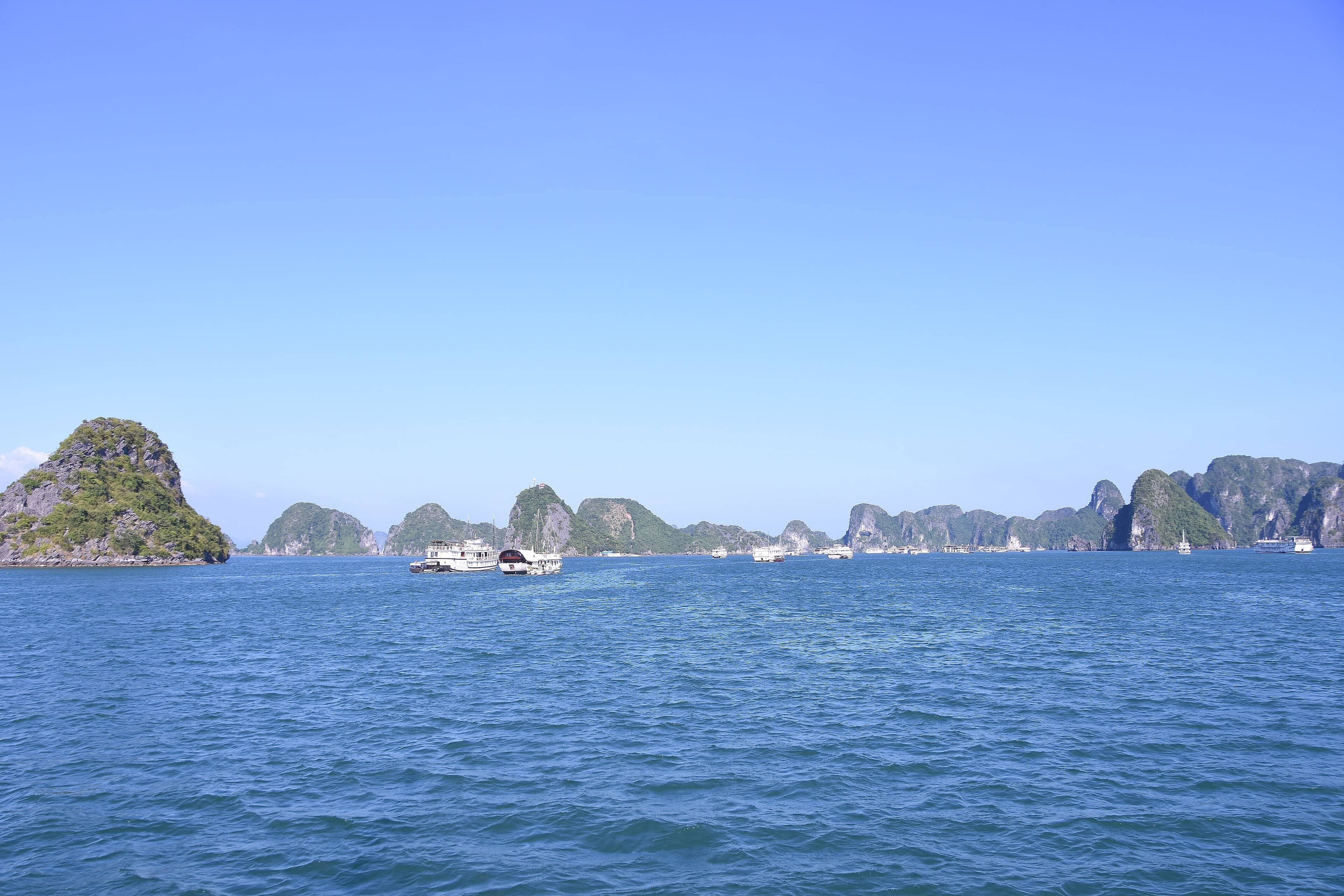 Limestone karst islands rising from the turquoise waters of Ha Long Bay under bright blue skies, Vietnam.z