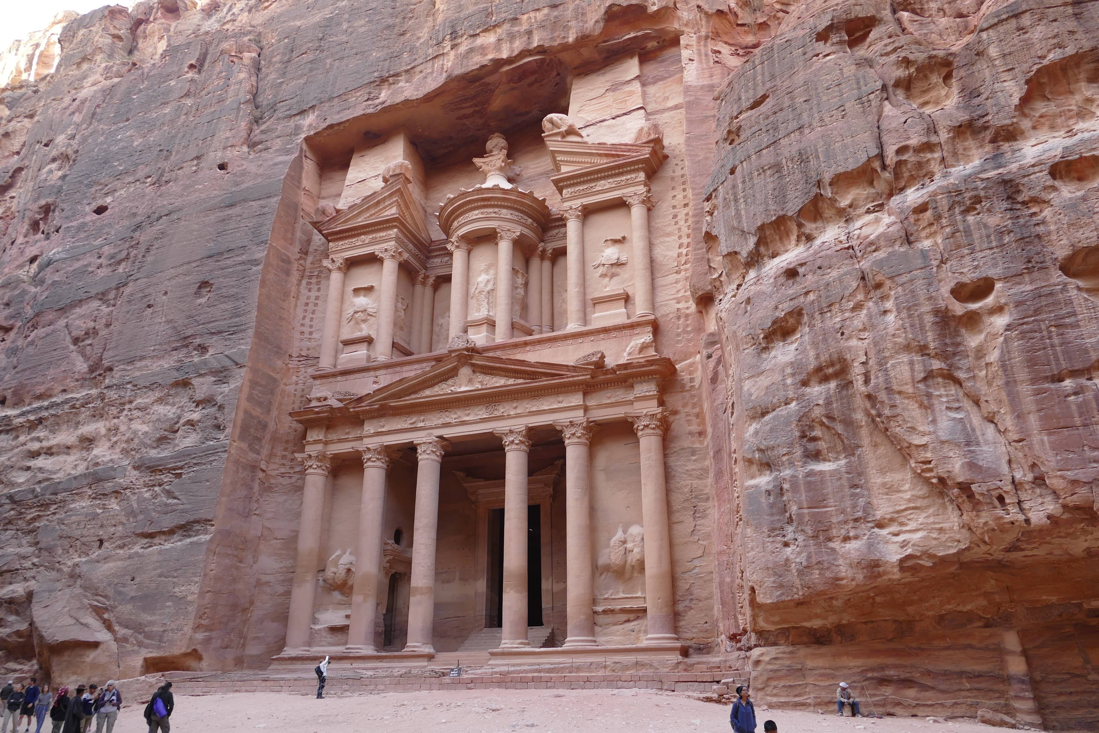 The rose-red Treasury facade at Petra, Jordan, lit by bright sunshine with visitors below.