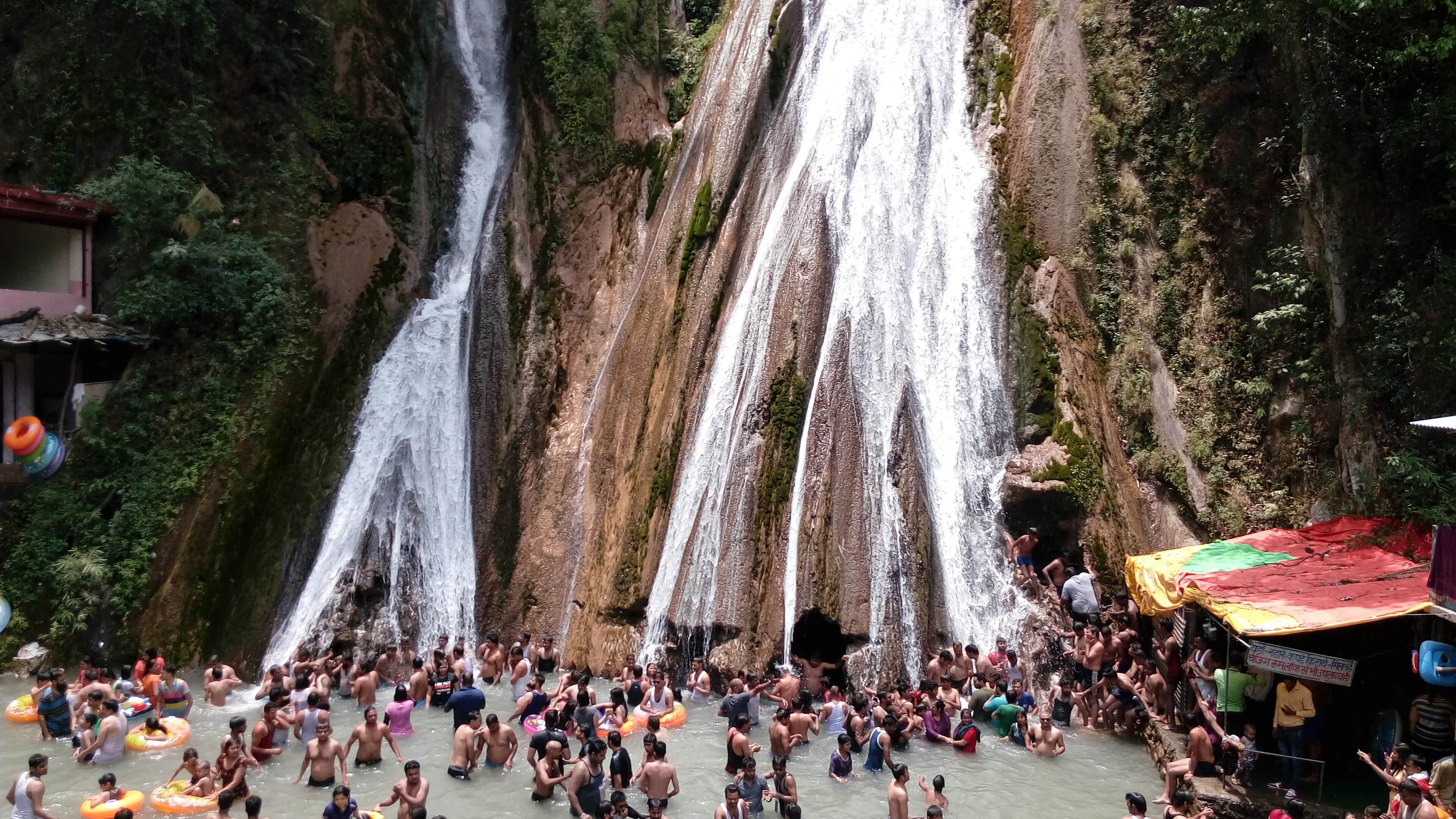 Visitors bathing in the pool beneath Kempty Falls near Mussoorie in bright sunshine.