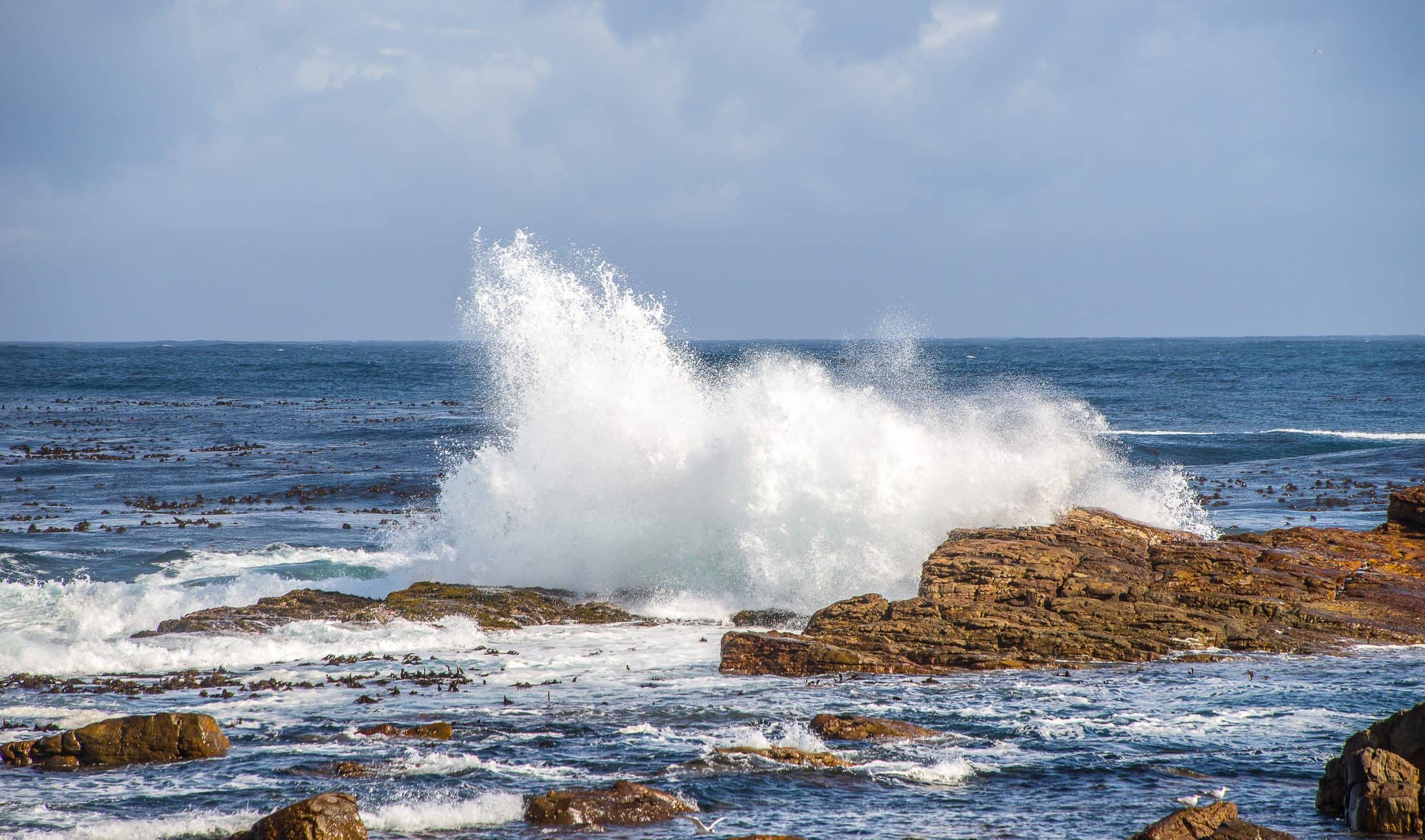 The rocks surrounded by the wavy sea under the sunlight and a cloudy sky at daytime in South Africa